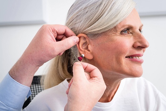 Ältere Frau erhält ein modernes Hörgerät von einem Hörakustiker für besseres Hören.